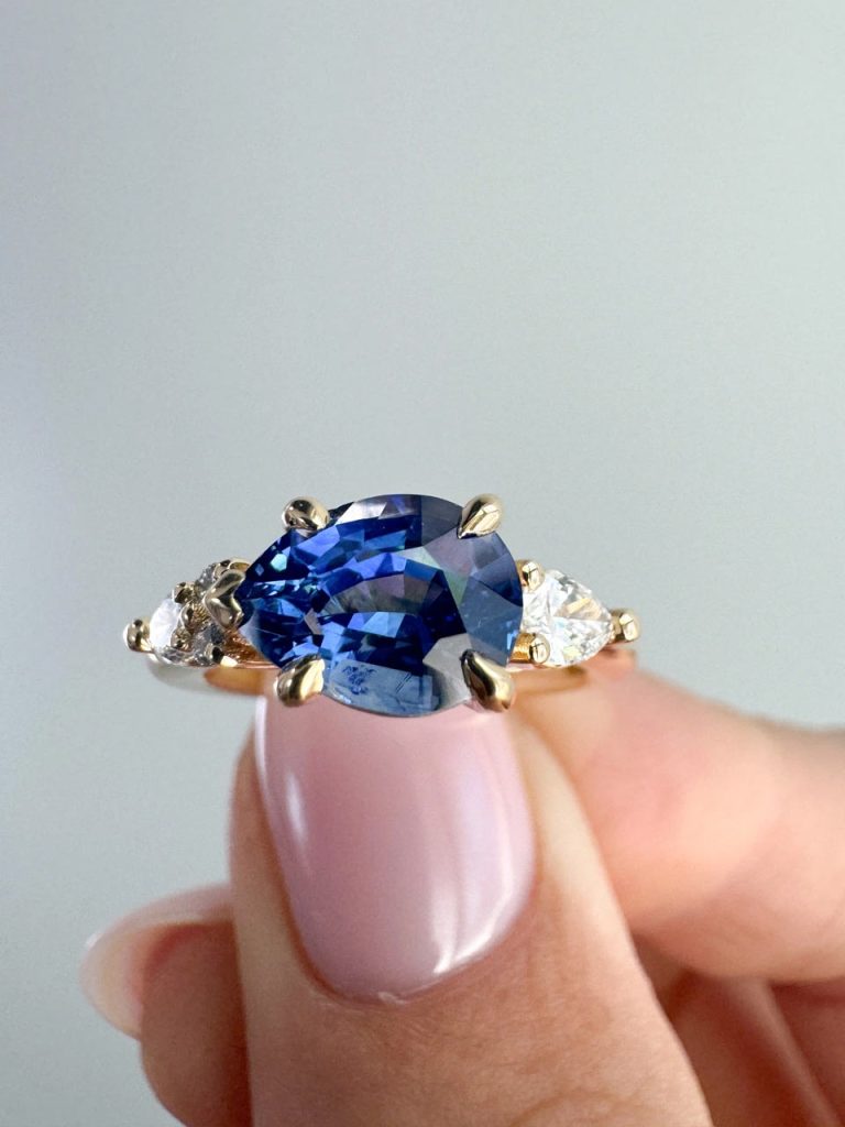 A large blue pear sapphire set in yellow gold, pointed prongs with smaller pear diamond accent stones, all set in an east-west setting